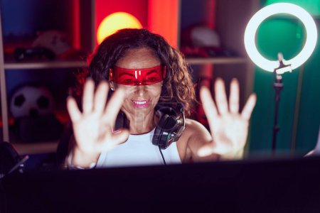 Téléchargez les photos : Femme du moyen âge streamer jouer à un jeu vidéo en utilisant des lunettes de réalité virtuelle à la salle de jeux - en image libre de droit