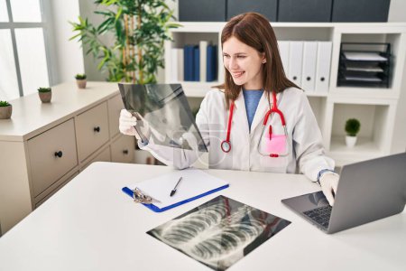 Foto de Mujer rubia joven médico buscando rayos X sentado en la mesa en la clínica - Imagen libre de derechos