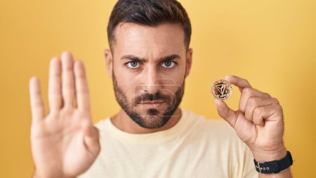 Photo for Handsome hispanic man holding tron cryptocurrency coin with open hand doing stop sign with serious and confident expression, defense gesture - Royalty Free Image