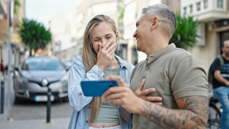 Téléchargez les photos : Homme et femme couple regarder la vidéo sur smartphone rire beaucoup à la rue - en image libre de droit