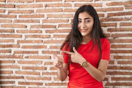 Photo for Young teenager girl standing over bricks wall pointing aside worried and nervous with both hands, concerned and surprised expression - Royalty Free Image
