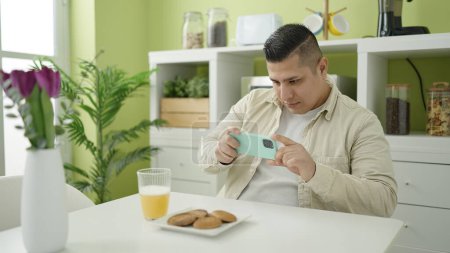 Téléchargez les photos : Jeune homme hispanique faire une photo par smartphone pour le petit déjeuner à la salle à manger - en image libre de droit