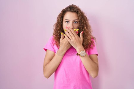 Foto de Joven mujer caucásica de pie sobre fondo rosa impactada cubriendo la boca con las manos por error. concepto secreto. - Imagen libre de derechos