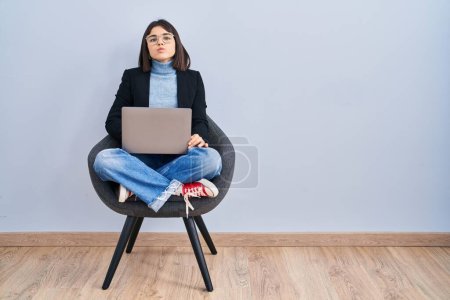 Photo for Young hispanic woman sitting on chair using computer laptop looking at the camera blowing a kiss on air being lovely and sexy. love expression. - Royalty Free Image