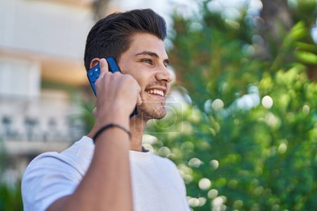 Téléchargez les photos : Jeune homme hispanique souriant confiant parler sur le smartphone au parc - en image libre de droit