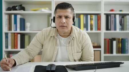 Téléchargez les photos : Jeune homme hispanique étudiant ayant écrit un appel vidéo sur le document à l'université de la bibliothèque - en image libre de droit