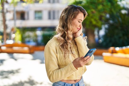 Téléchargez les photos : Jeune femme utilisant un smartphone avec une expression détendue au parc - en image libre de droit