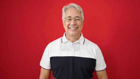 Téléchargez les photos : Homme d'âge moyen aux cheveux gris souriant confiant sur fond rouge isolé - en image libre de droit