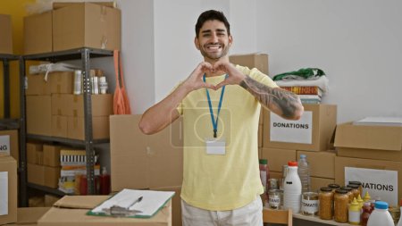 Téléchargez les photos : Jeune homme hispanique volontaire souriant confiant faire geste de cœur au centre de charité - en image libre de droit
