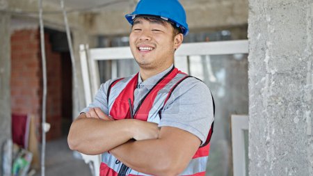 Téléchargez les photos : Constructeur souriant confiant debout avec les bras croisés geste sur le chantier de construction - en image libre de droit