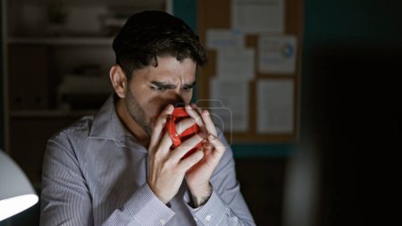 Foto de Trabajador de negocios hispano joven bebiendo una taza de café trabajando en la oficina - Imagen libre de derechos