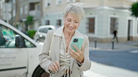 Photo for Middle age blonde woman smiling confident using smartphone at street - Royalty Free Image