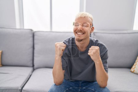Téléchargez les photos : Jeune homme caucasien portant des lunettes de réalité virtuelle très heureux et excité de faire geste gagnant avec les bras levés, souriant et criant pour le succès. concept de célébration. - en image libre de droit
