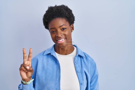 Téléchargez les photos : Femme afro-américaine debout sur fond bleu montrant et pointant vers le haut avec les doigts numéro deux tout en souriant confiant et heureux. - en image libre de droit