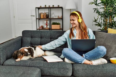 Photo for Young caucasian woman sitting on sofa with dog studying at home - Royalty Free Image