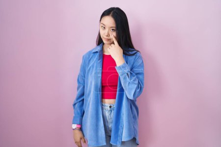 Téléchargez les photos : Jeune femme asiatique debout sur fond rose pointant vers l'œil vous regardant geste, expression suspecte - en image libre de droit
