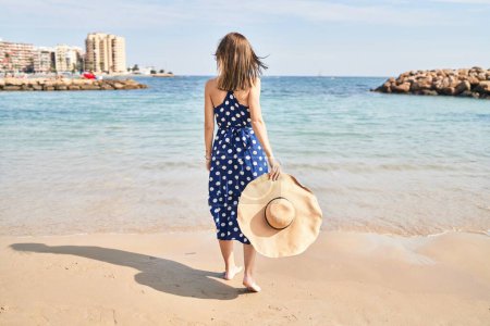 Photo for Young blonde woman tourist holding summer hat walking at beach - Royalty Free Image