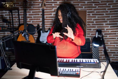 Téléchargez les photos : Plus taille hispanique femme jouant du piano au studio de musique expression dégoûtée, mécontent et peur de faire face dégoût parce que la réaction d'aversion. les mains levées - en image libre de droit