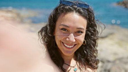 Foto de Joven hermosa mujer hispana turista sonriendo confiada teniendo videollamada besándose en la playa - Imagen libre de derechos