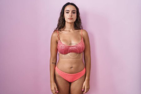 Photo for Young hispanic woman wearing lingerie over pink background relaxed with serious expression on face. simple and natural looking at the camera. - Royalty Free Image
