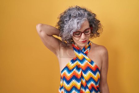 Photo for Middle age woman with grey hair standing over yellow background suffering of neck ache injury, touching neck with hand, muscular pain - Royalty Free Image
