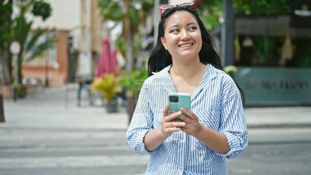 Téléchargez les photos : Jeune femme chinoise utilisant smartphone souriant à la rue - en image libre de droit
