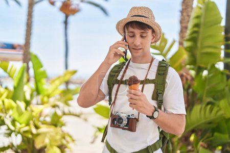 Foto de Young caucasian man tourist talking on smartphone eating ice cream at park - Imagen libre de derechos
