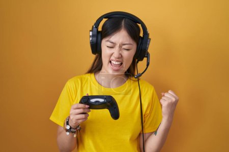 Photo for Chinese young woman playing video game holding controller very happy and excited doing winner gesture with arms raised, smiling and screaming for success. celebration concept. - Royalty Free Image