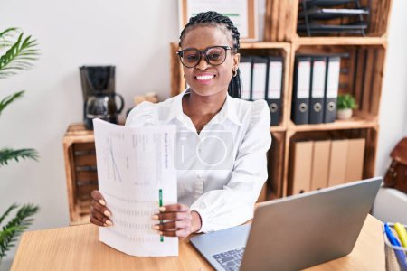 Téléchargez les photos : Femme afro-américaine travailleur d'affaires en utilisant un document de détention d'ordinateur portable au bureau - en image libre de droit