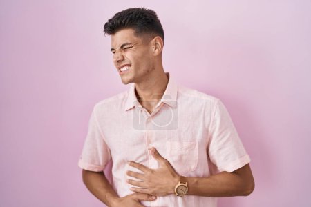 Téléchargez les photos : Jeune homme hispanique debout sur fond rose avec la main sur le ventre parce que l'indigestion, la maladie douloureuse se sent mal. concept de douleur. - en image libre de droit