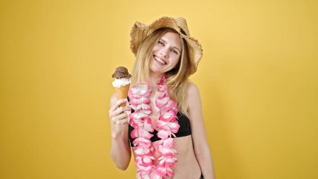 Photo for Young blonde woman tourist wearing bikini and hawaiian lei holding ice cream over isolated yellow background - Royalty Free Image