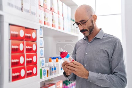 Foto de Joven cliente hispano sonriendo confiado sosteniendo la botella de medicación en la farmacia - Imagen libre de derechos