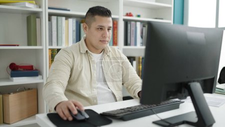 Foto de Young hispanic man student using computer studying at library university - Imagen libre de derechos