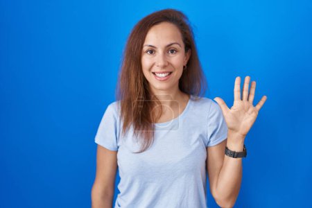 Photo for Brunette woman standing over blue background showing and pointing up with fingers number five while smiling confident and happy. - Royalty Free Image