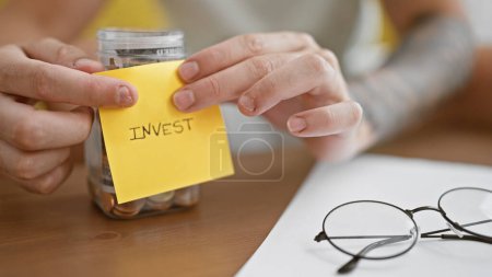 Photo for Young hispanic man putting invest reminder paper on bottle with money at park - Royalty Free Image