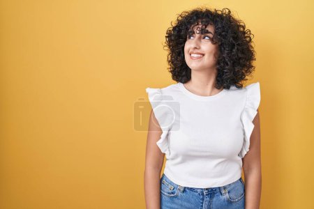 Foto de Joven mujer de Oriente Medio de pie sobre fondo amarillo sonriendo mirando a un lado y mirando hacia otro pensando. - Imagen libre de derechos
