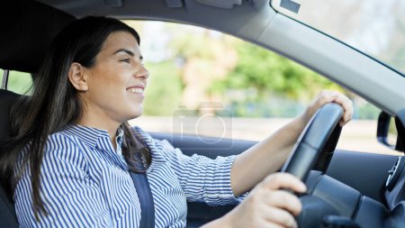 Young beautiful hispanic woman driving a car smiling on the road