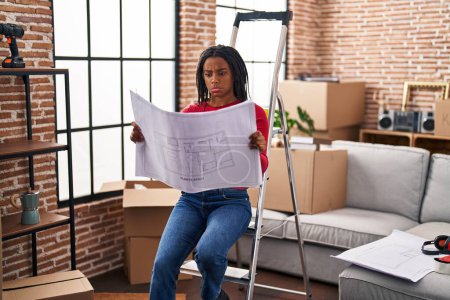 Photo for Young african american with braids standing on new home looking at blueprints depressed and worry for distress, crying angry and afraid. sad expression. - Royalty Free Image