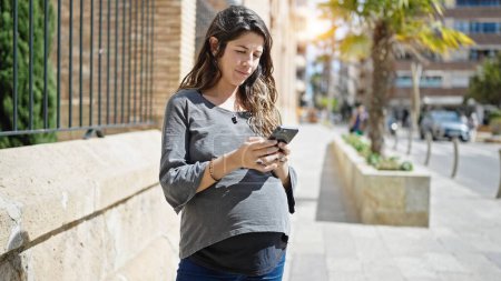 Photo for Young pregnant woman using smartphone at street - Royalty Free Image