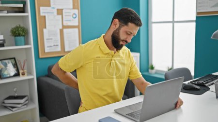 Téléchargez les photos : Jeune homme hispanique travailleur d'affaires utilisant ordinateur portable souffrant de maux de dos au bureau - en image libre de droit
