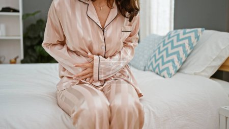 Photo for Young woman suffering for menstrual pain sitting on bed at bedroom - Royalty Free Image
