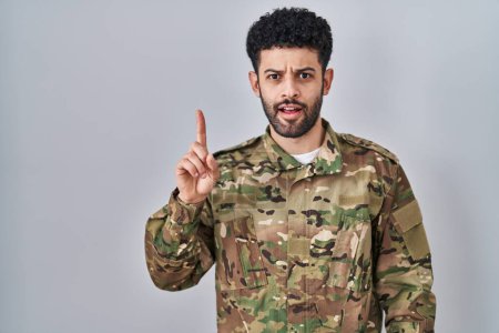 Foto de Hombre árabe con camuflaje uniforme del ejército apuntando con el dedo hacia arriba con una idea exitosa. exitado y feliz. número uno. - Imagen libre de derechos