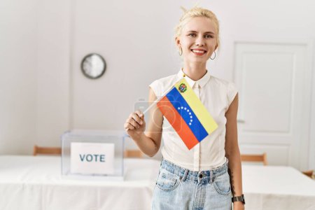Téléchargez les photos : Jeune femme blonde tenant le drapeau venezuela souriant au collège électoral - en image libre de droit