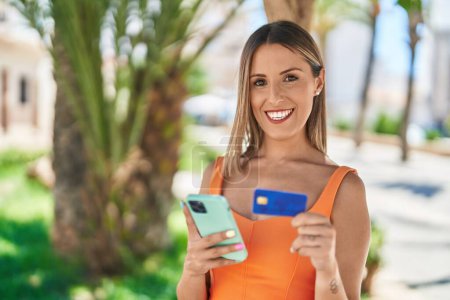 Foto de Joven mujer hispana hermosa usando teléfono inteligente y tarjeta de crédito en el parque - Imagen libre de derechos