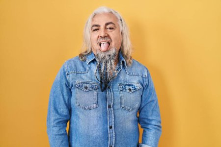 Téléchargez les photos : Homme du moyen âge avec les cheveux gris debout sur fond jaune langue collante heureux avec une expression drôle. concept d'émotion. - en image libre de droit