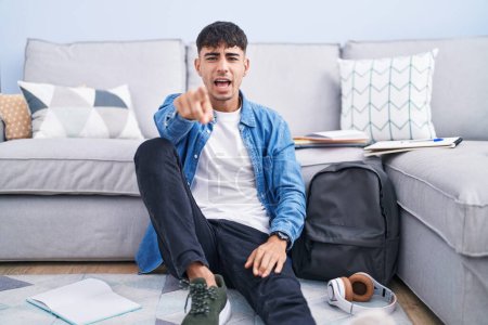 Photo for Young hispanic man sitting on the floor studying for university pointing displeased and frustrated to the camera, angry and furious with you - Royalty Free Image