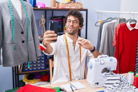 Foto de Young hispanic man tailor smiling confident having video call at clothing factory - Imagen libre de derechos