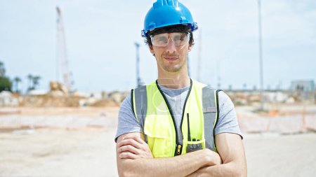 Photo for Young hispanic man architect standing with arms crossed gesture and serious face at construction place - Royalty Free Image