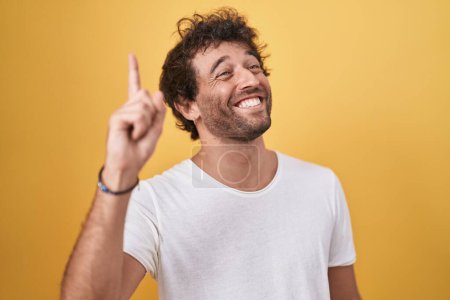 Foto de Young hispanic man smiling confident doing idea gesture with finger over isolated yellow background - Imagen libre de derechos