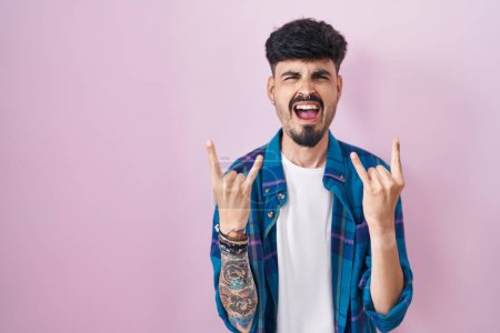 Photo for Young hispanic man with beard standing over pink background shouting with crazy expression doing rock symbol with hands up. music star. heavy concept. - Royalty Free Image